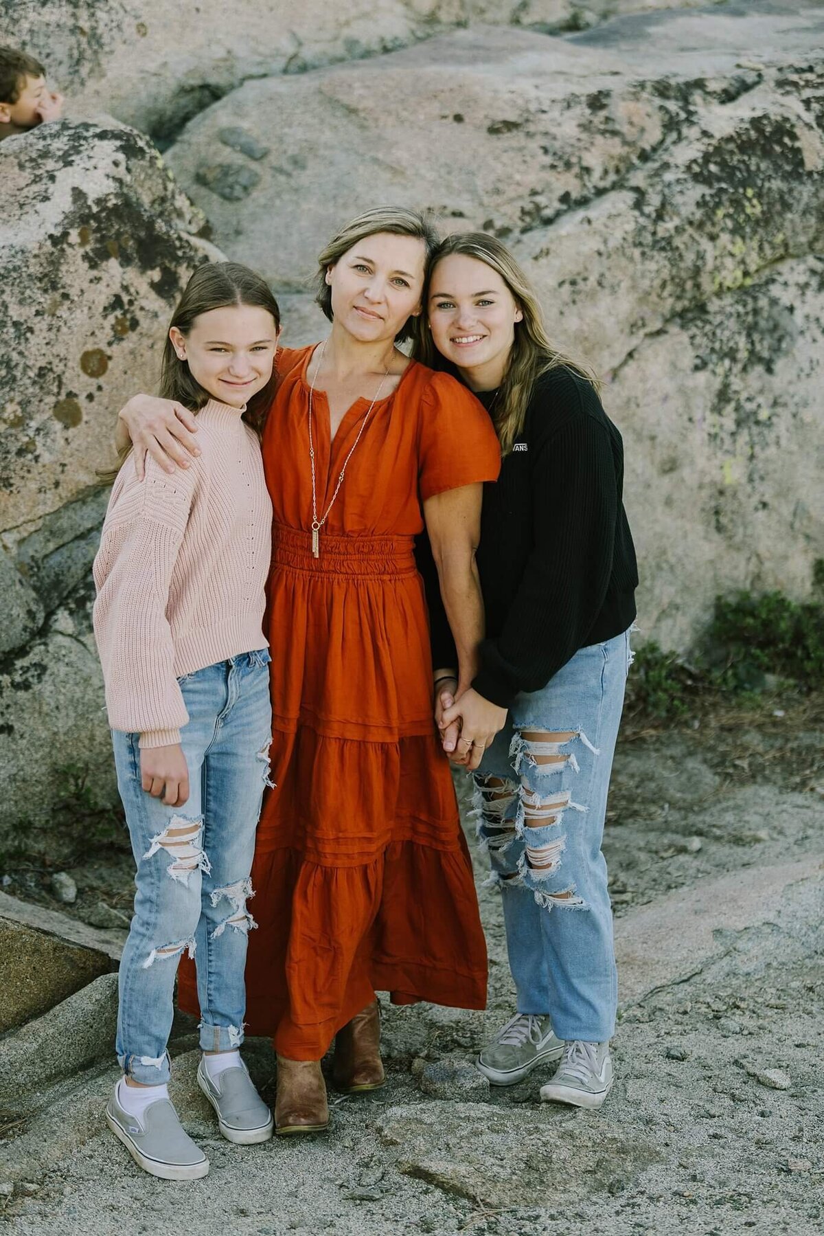 vertical image of mom and teenage daughters with granite rocks behind them during portraits on donner summit