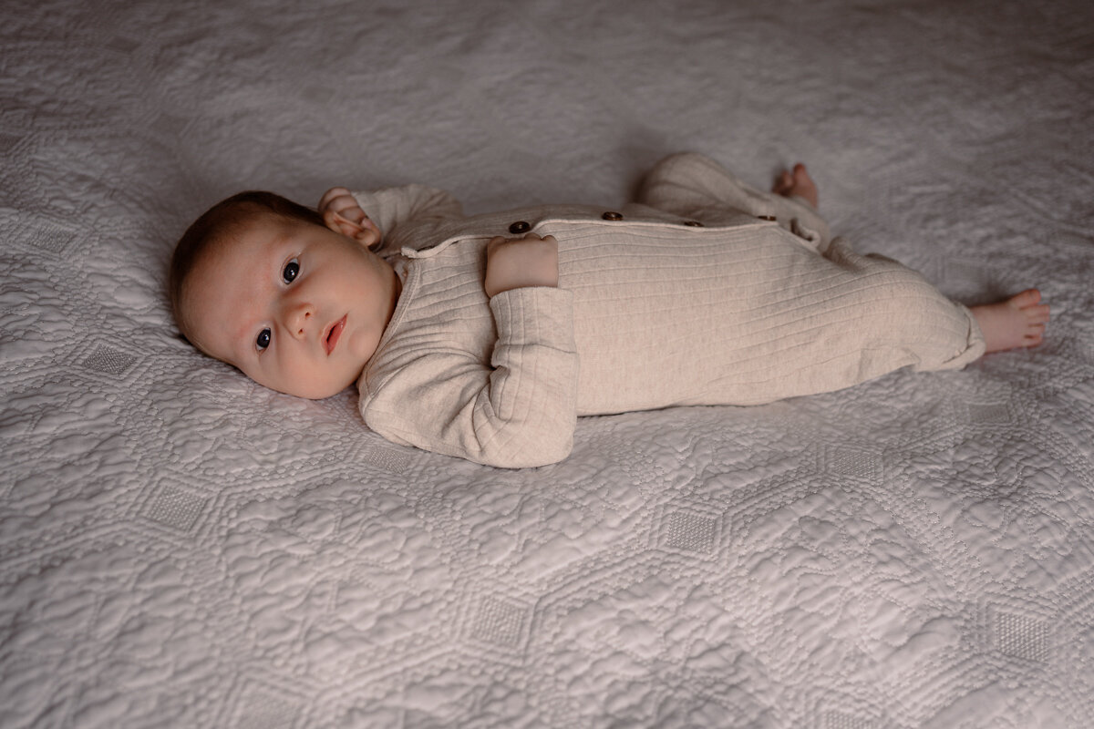 pasgeboren baby ligt op het bed rond te kijken tijdens een newbornshoot