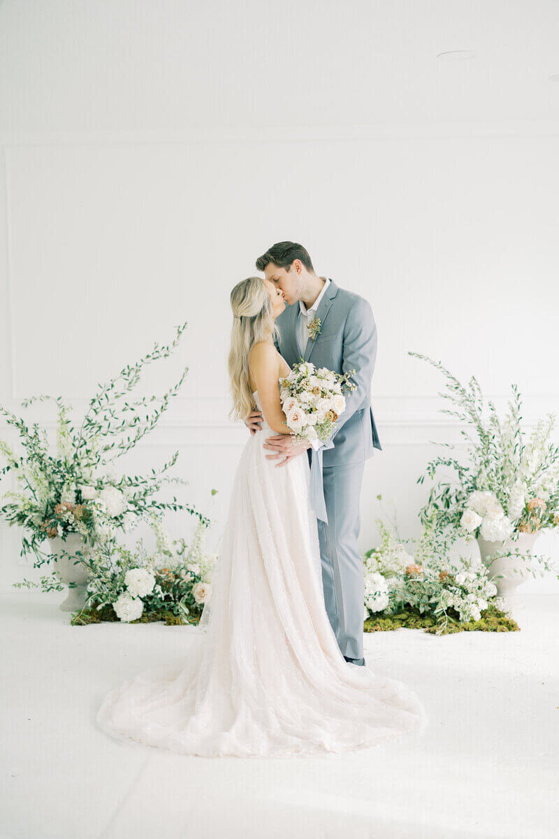 Bride and groom kissing with flowers behind them designed by wedding planners chicago