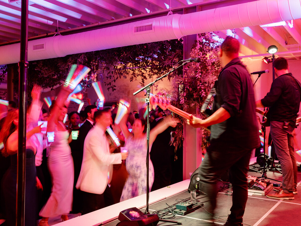 A lively wedding reception featuring a live band, enthusiastic guests dancing, and colorful lights creating a joyous atmosphere showcasing celebration and connection.