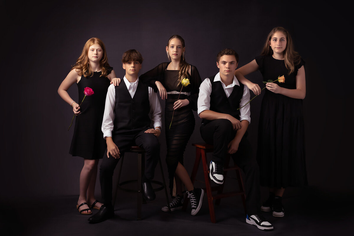 A group of five friends in coordinated black outfits, each holding a different colored rose, exuding a stylish and artistic vibe. A Dallas senior photographer captures the essence of friendship in a chic, modern portrait.