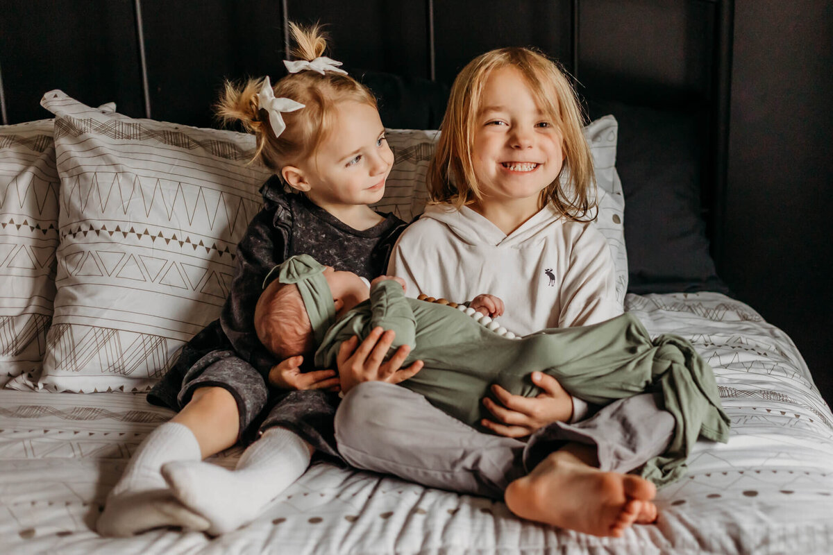 brother and sister holding baby on bed with luci levon photography