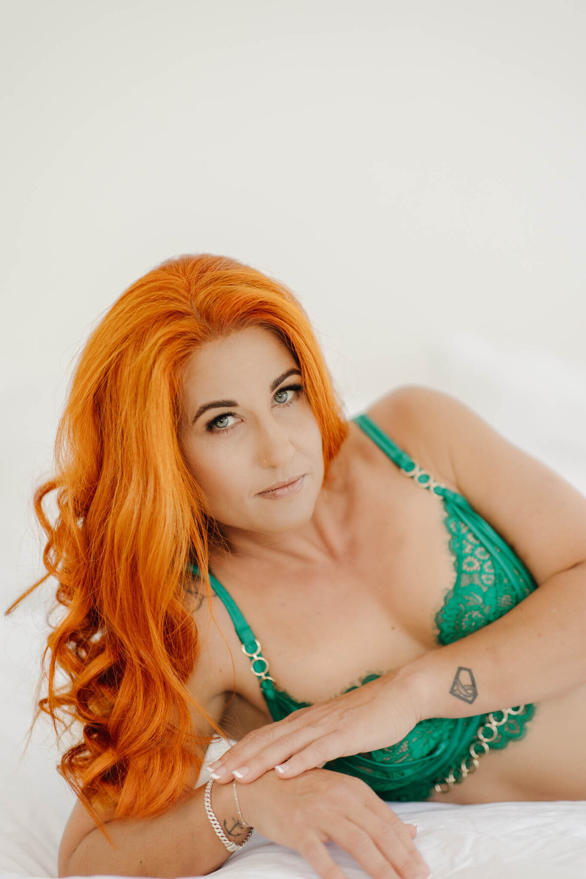 woman with vibrant hair in green lingerie stares into camera of boudoir session in mackay.