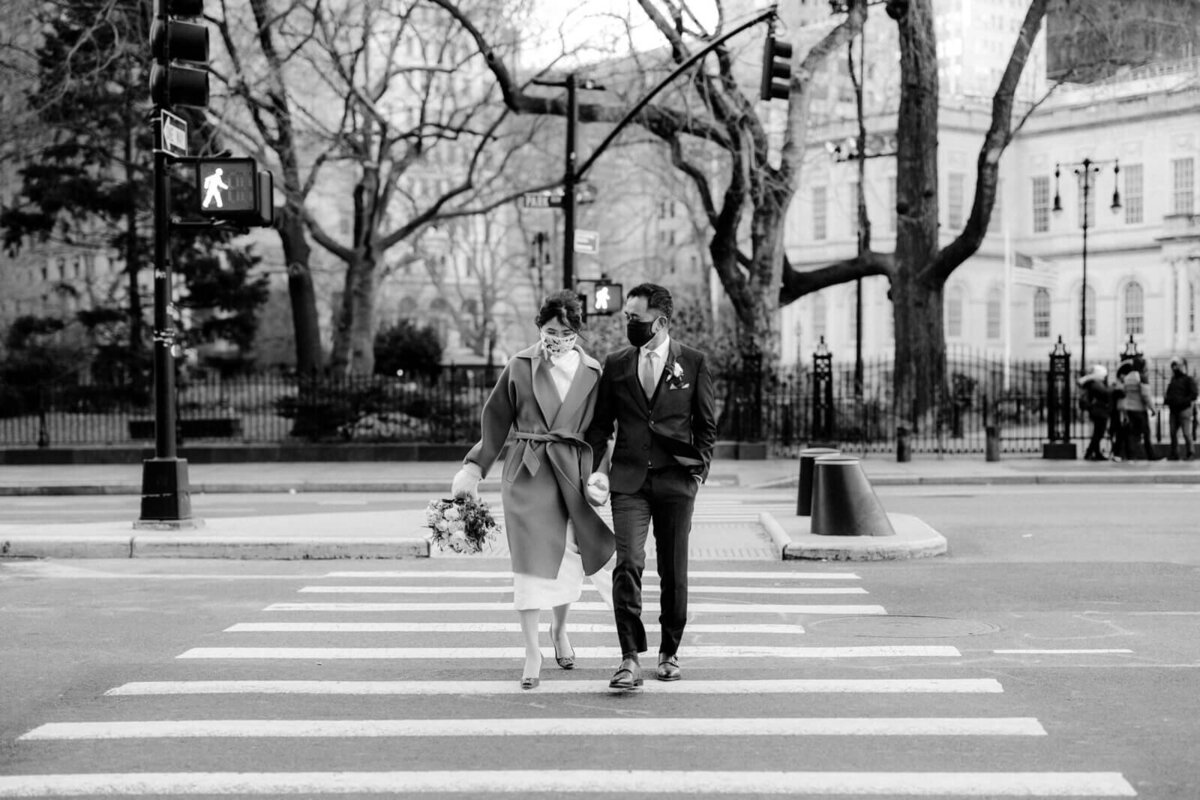 Black and white photo of the bride and groom wearing face masks while crossing a pedestrian lane in New York City.
