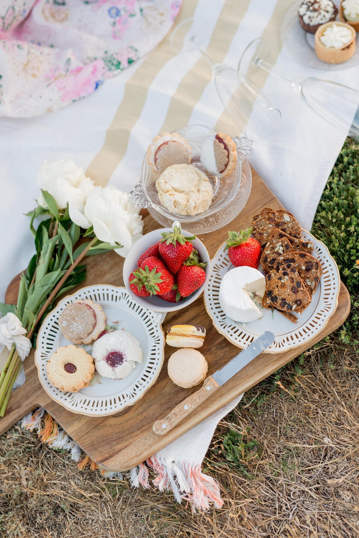 Charming picnic flatlay with strawberries, cookies, brie, and florals—sweet, romantic, and perfectly styled for an engagement shoot.