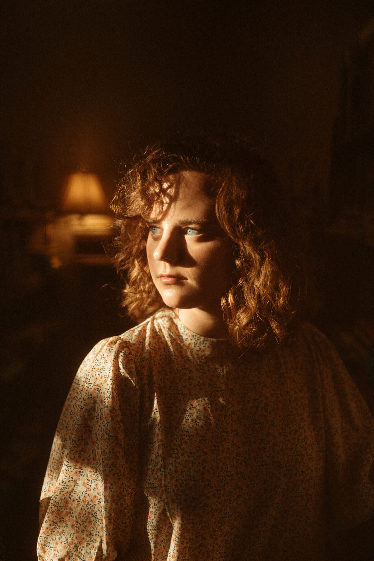 Senior with short naturally curly hair looking out a window in dramatic lighting