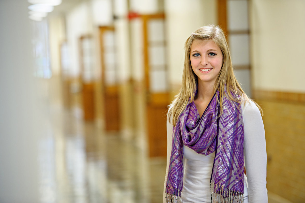 A young confident professional woman stands in a hallway of open doors.