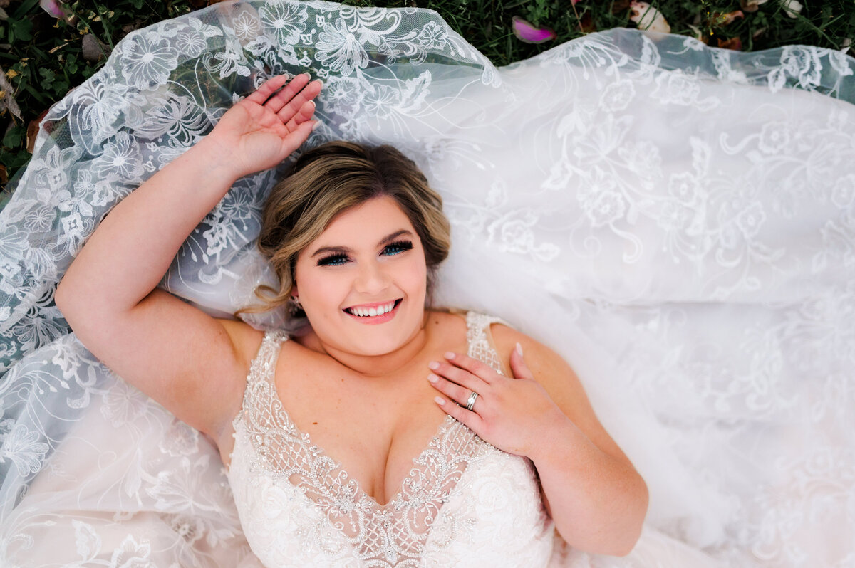 bride laying on the ground with her lace wedding dress behind her in a garden