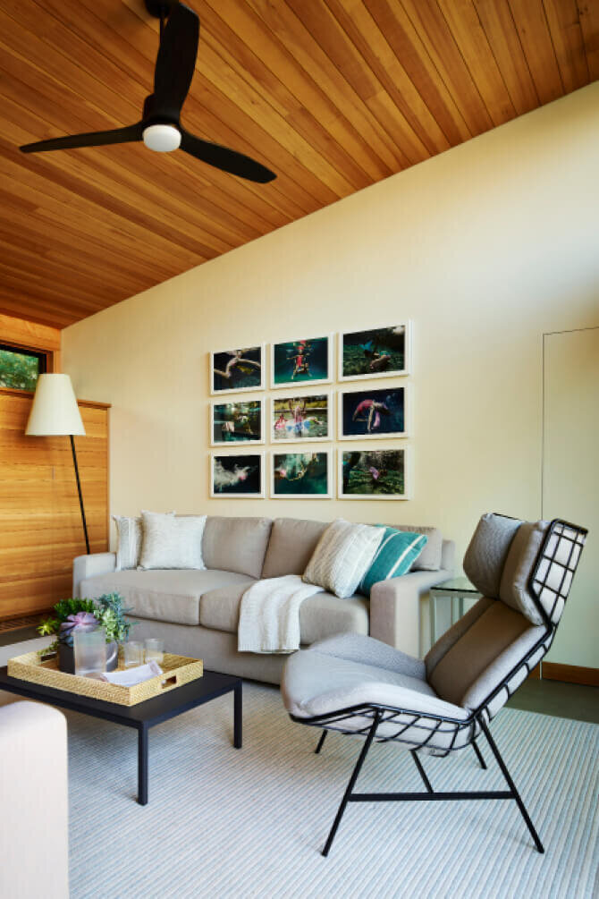 Modern living room design by interior designers in Hingham features luxury furniture, personal art, and red cedar siding and ceiling for a warm, refined space.