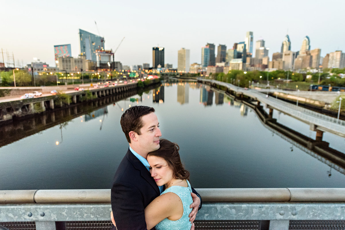 A gorgeous couple hold each other on south street bridge with the philadelphia skyline in the background.