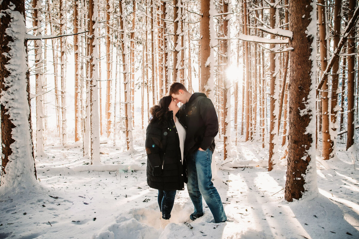man and woman stand forehead to forehead in a snowy forest