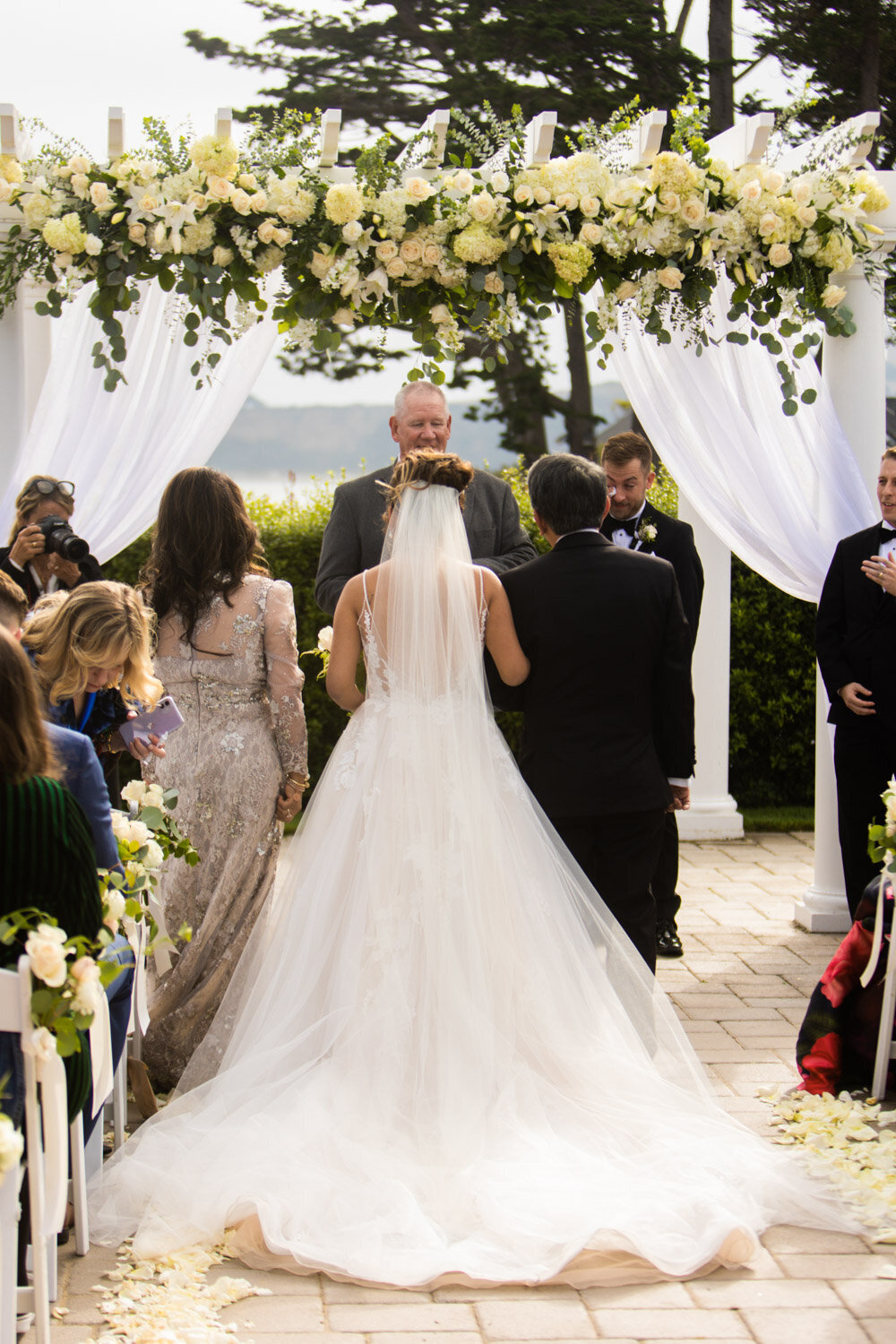 Outdoor wedding ceremony with white draped arch and floral arrangements
