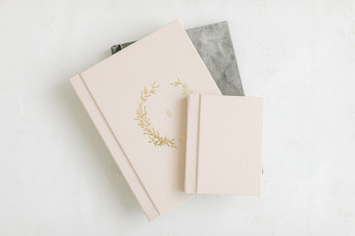 A grey linen covered heirloom album with two cream linen covered heirloom albums lay atop each other showing the various covers and sizes of albums available to display your Indianapolis boudoir photos.