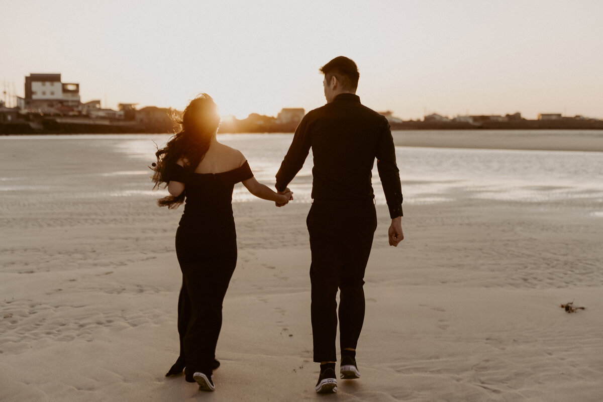 the couple holding hands while walking in the shore  under the golden sunset in Jeju Island