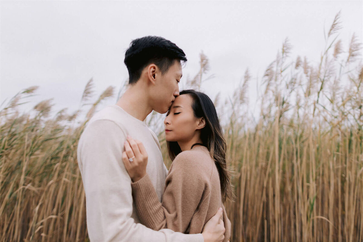 The engaged couple is romantically hugging in the midst of the tall grasses in New York. Engagement Image by Jenny Fu Studio