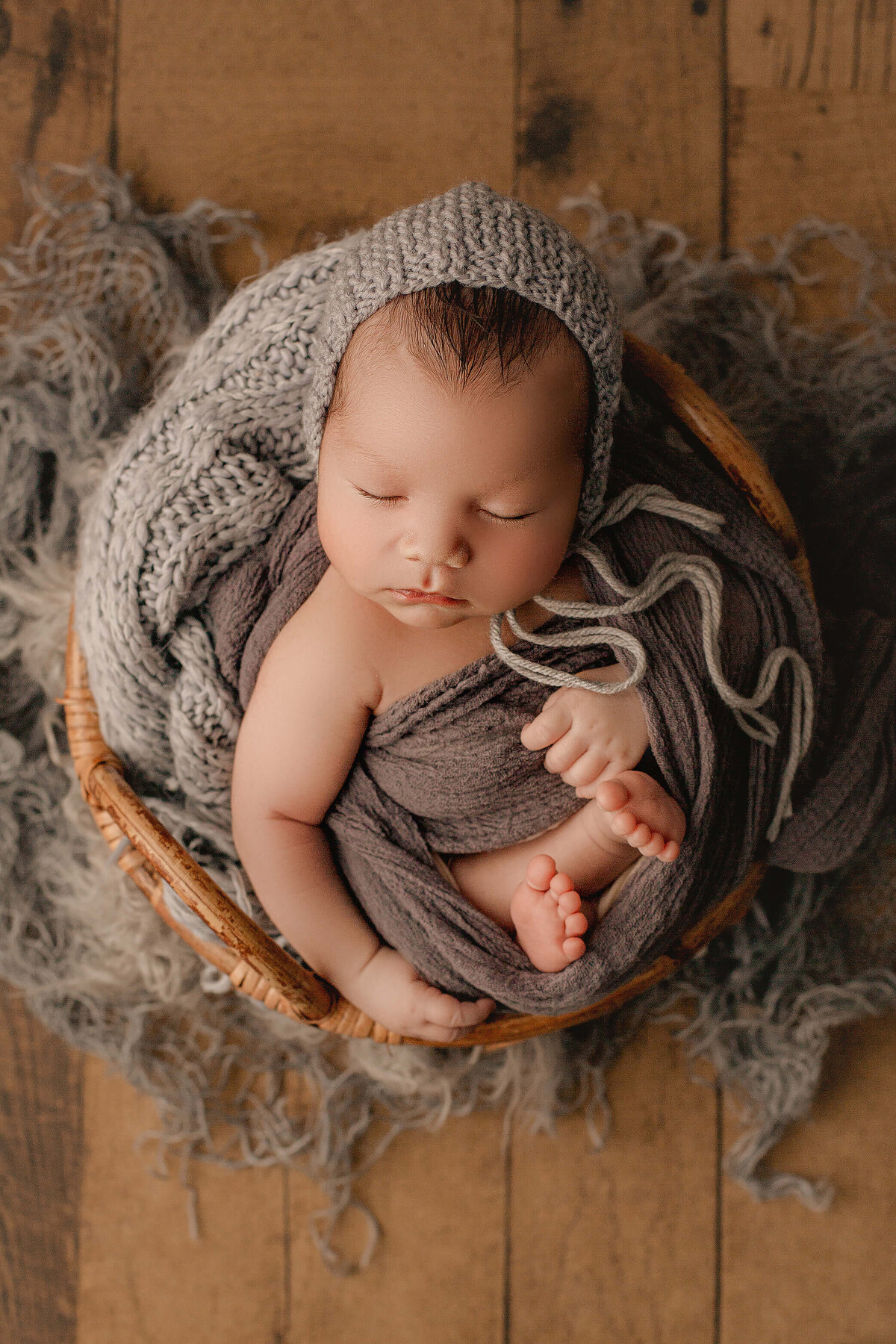 hamilton newborn photographer captures baby boy wrapped in grey cloth, sleeping in a bamboo basket