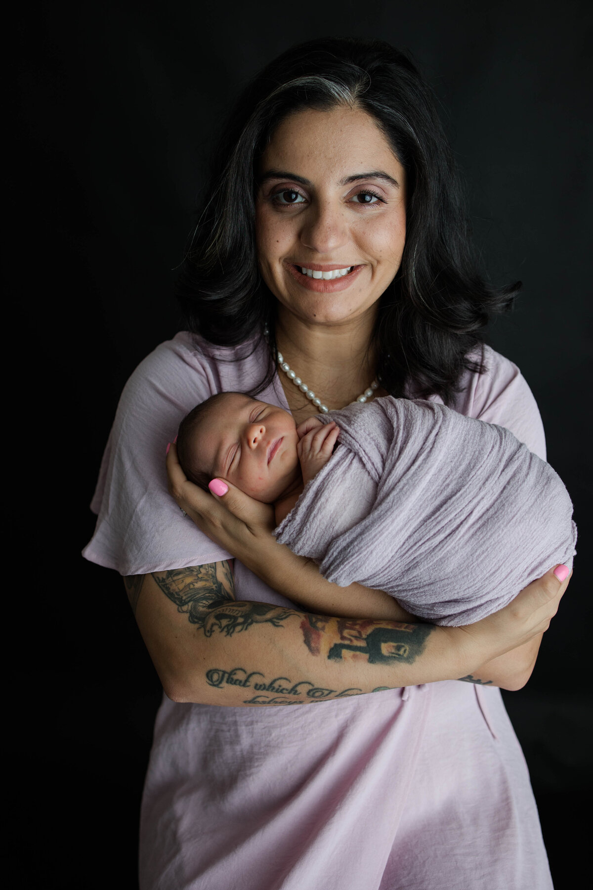 Newborn baby girl wrapped in a purple blanket with her mom holding her and smiling