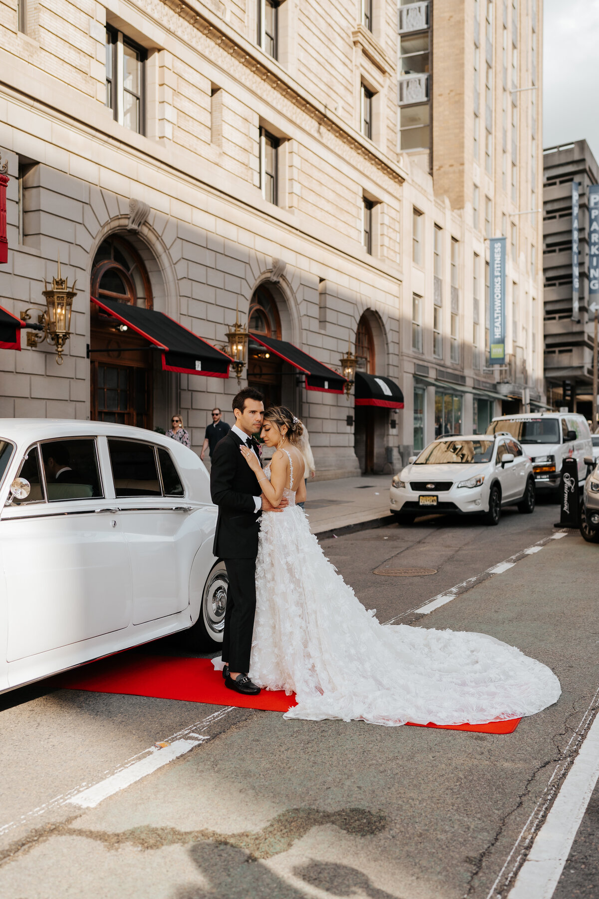 bride and groom embracing while leaning against old white car in the street
