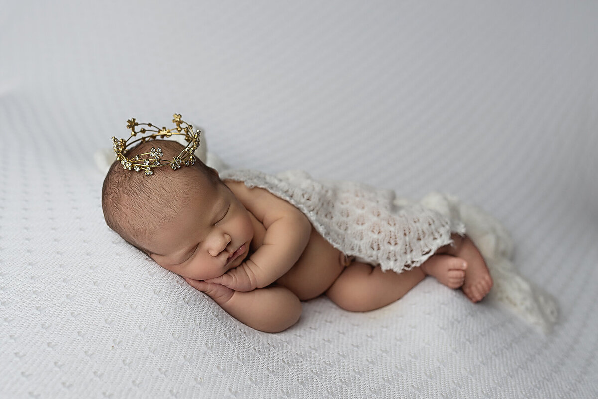 A lace blanket covers a sleeping newborn baby wearing a golden crown