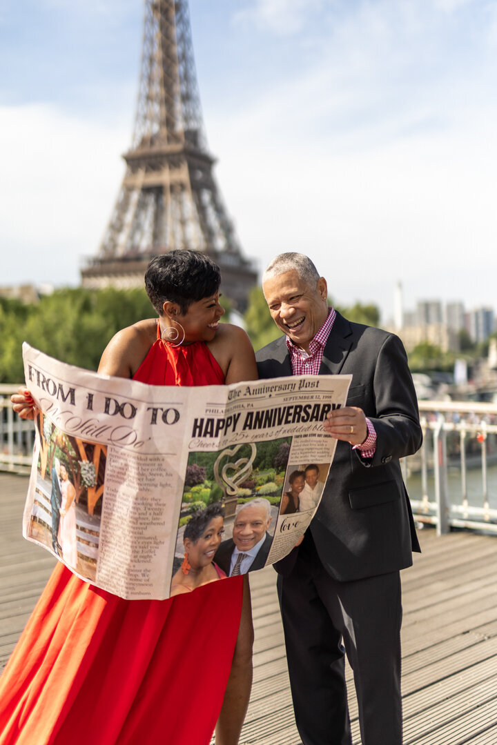 Anniversary couple photoshoot Paris, candid laughing moment, Happy Anniversary newspaper prop, Eiffel Tower backdrop