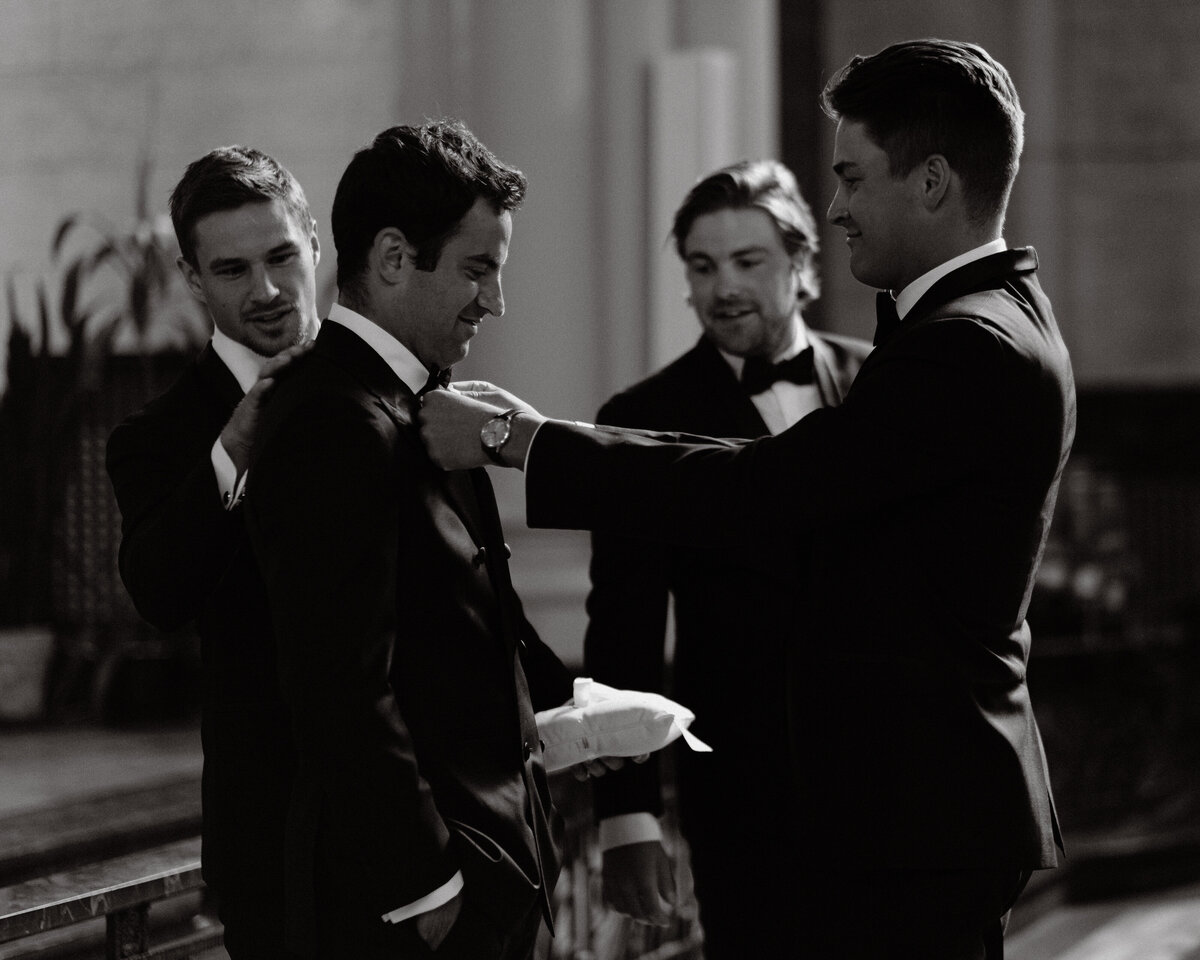 groomsmen fix up the groom's tie while he waits for his future wife