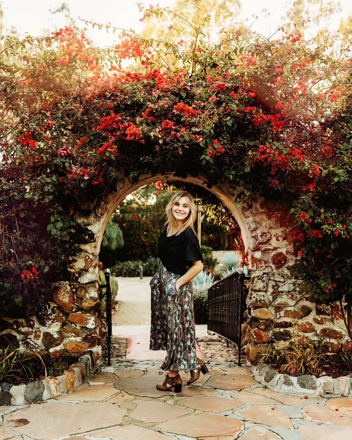 High school senior girl leaning in a floral arch at sunset.