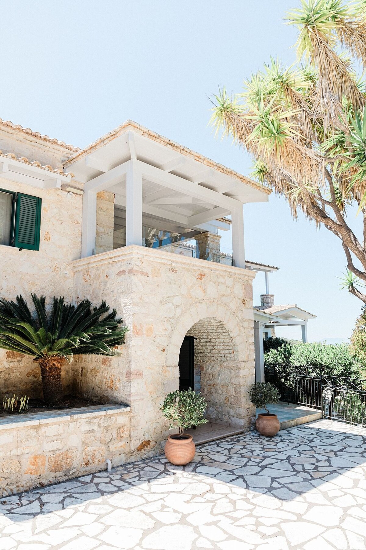 Stone villa with arched entryway, potted plants, and shaded terrace