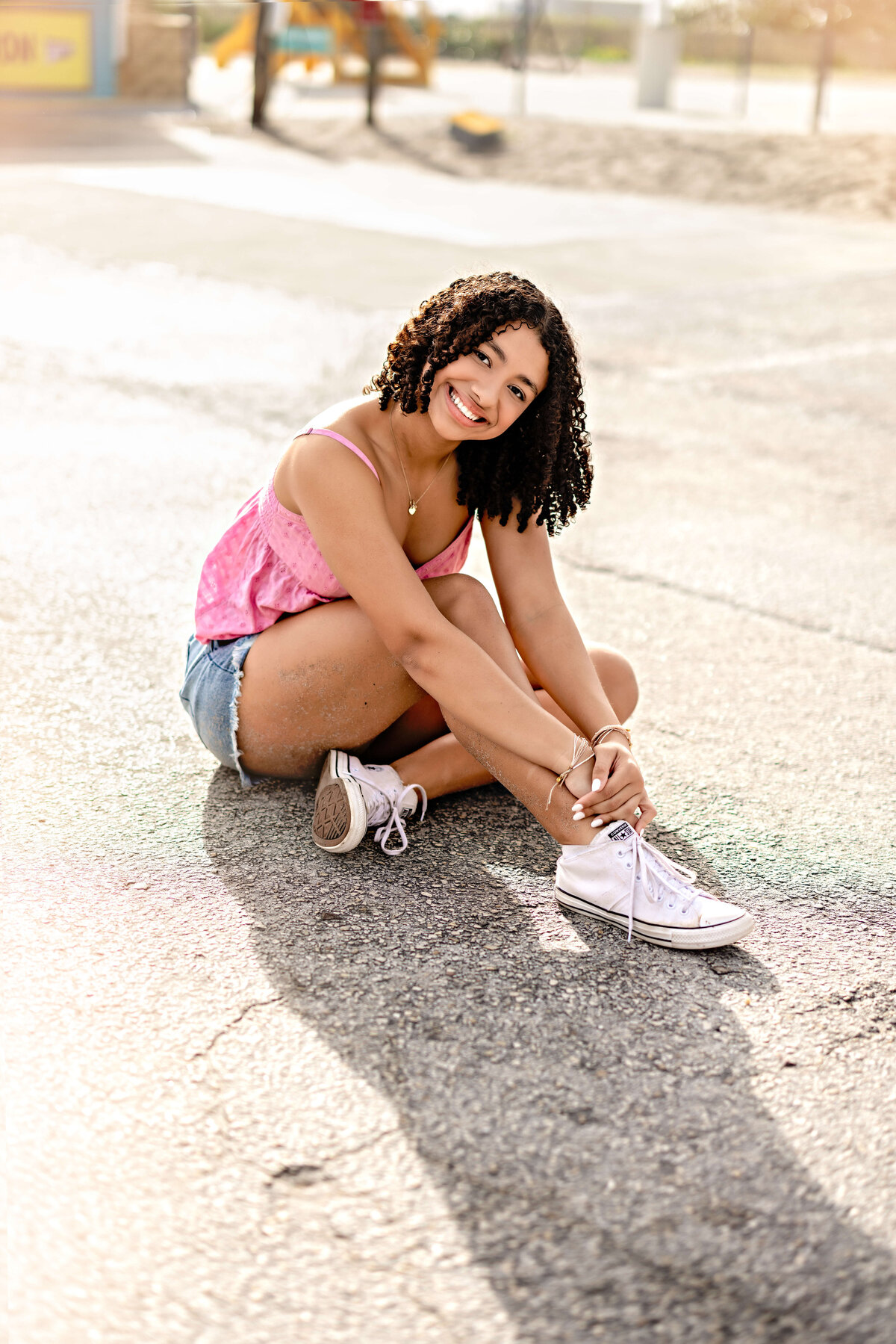 Senior portrait on a sunlit parking lot near Cocoa Beach, side angled with golden light highlighting her soft curls and natural expression.