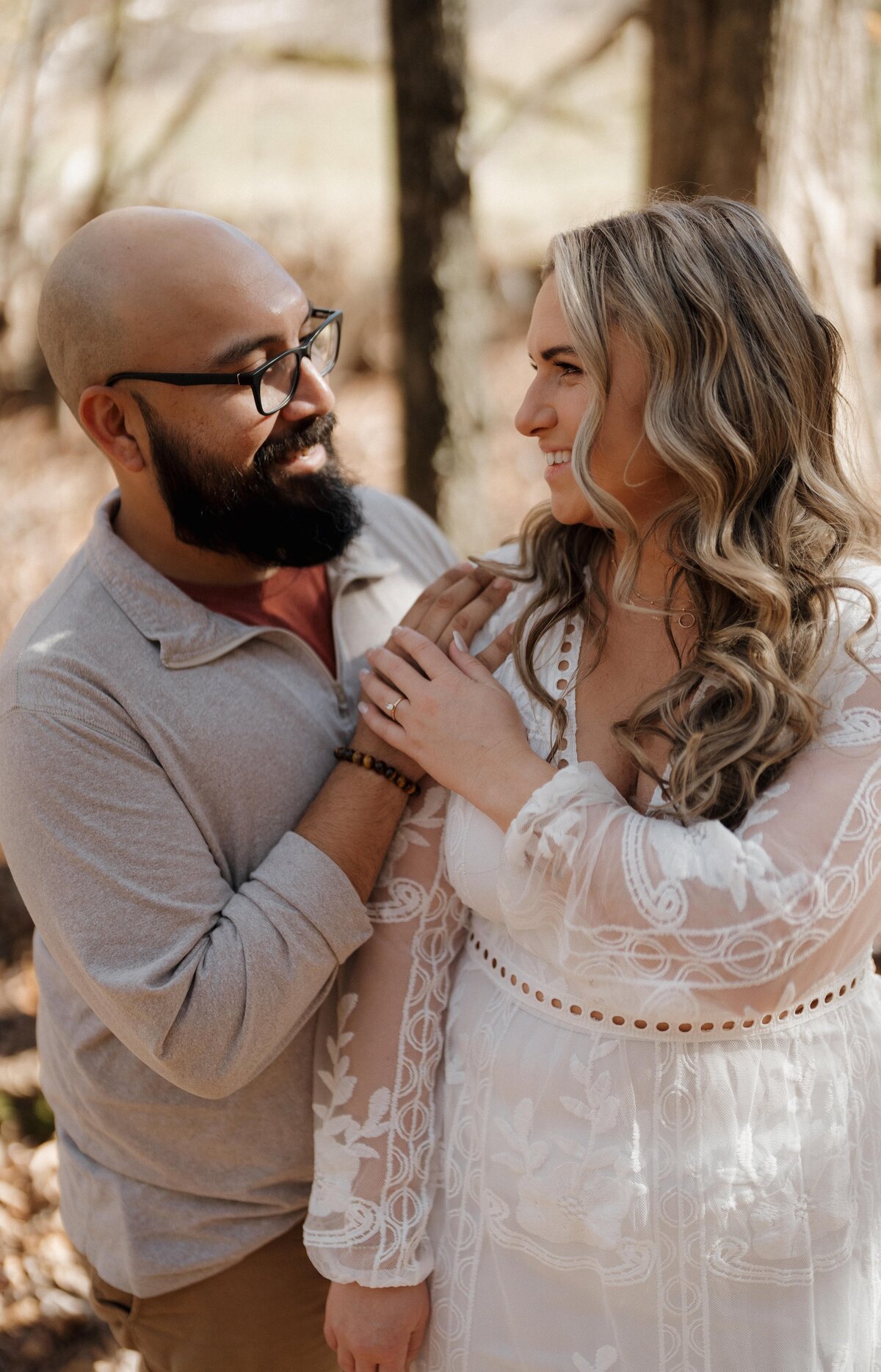 Couple walking hand-in-hand in the woods, smiling at each other