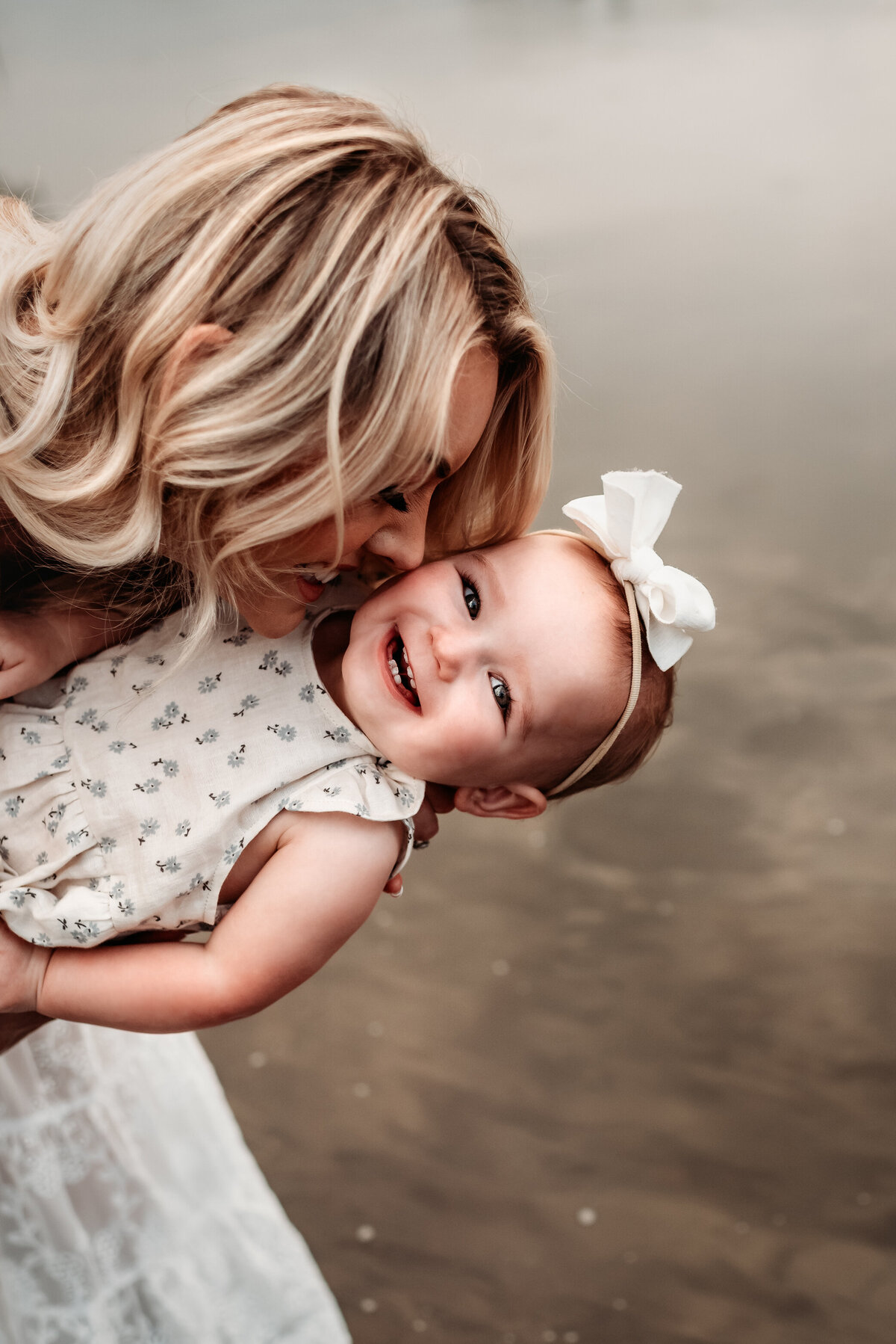 mom dipping her daughter near the river and snuggling her cheek