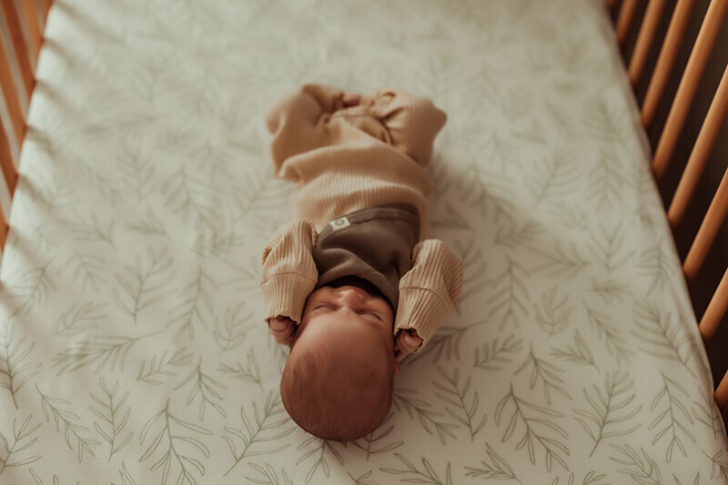 Newborn baby in khaki sleeper sleeping in his crib