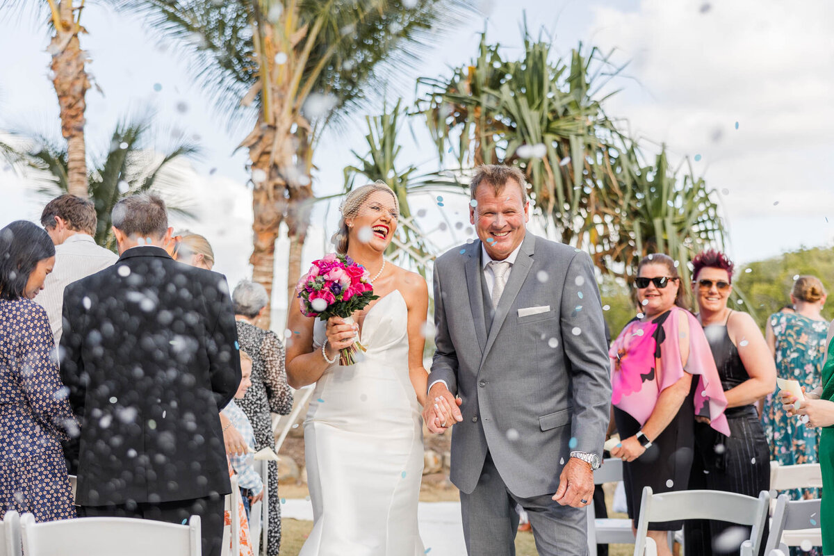 Bride and groom, hold hands as they walk back down the aisle at the tropical Whitsunday wedding venue