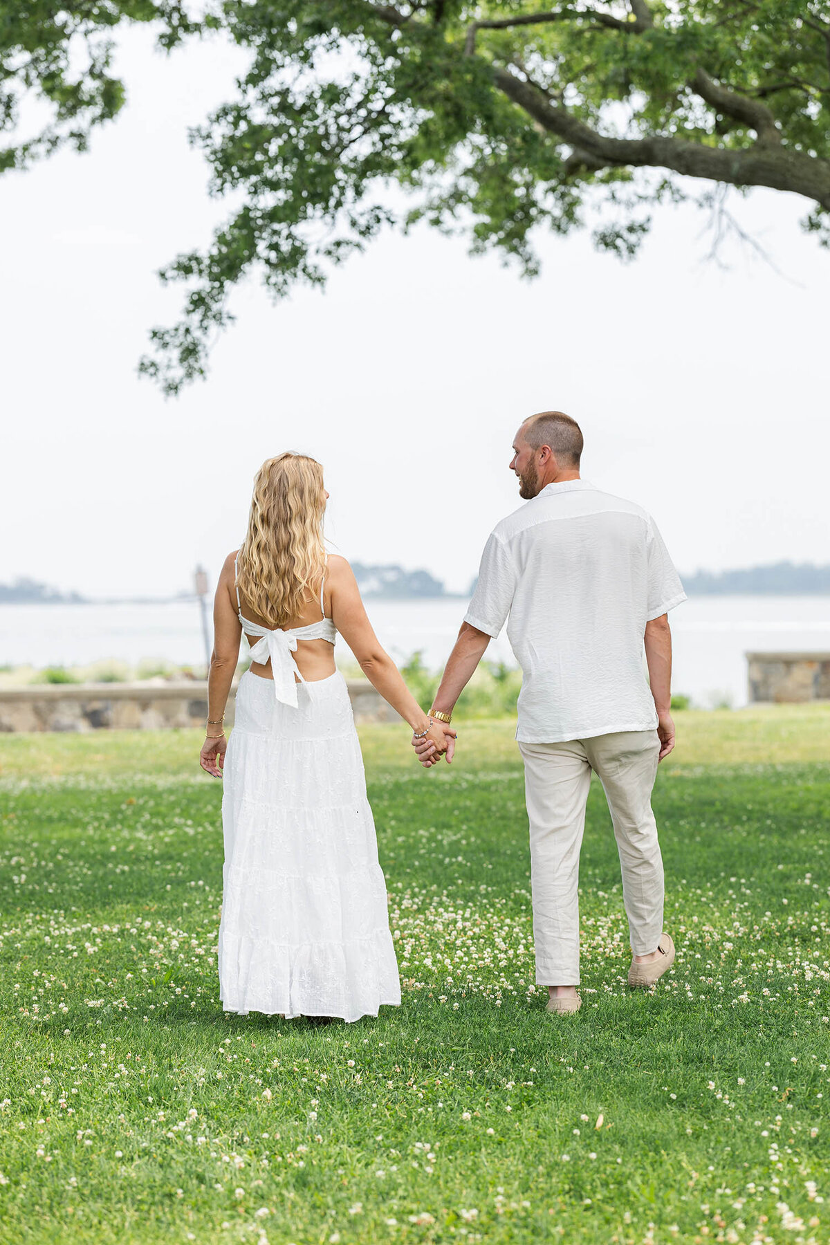Couple holding hands near the shoreline as they walk towards the sea wall. 