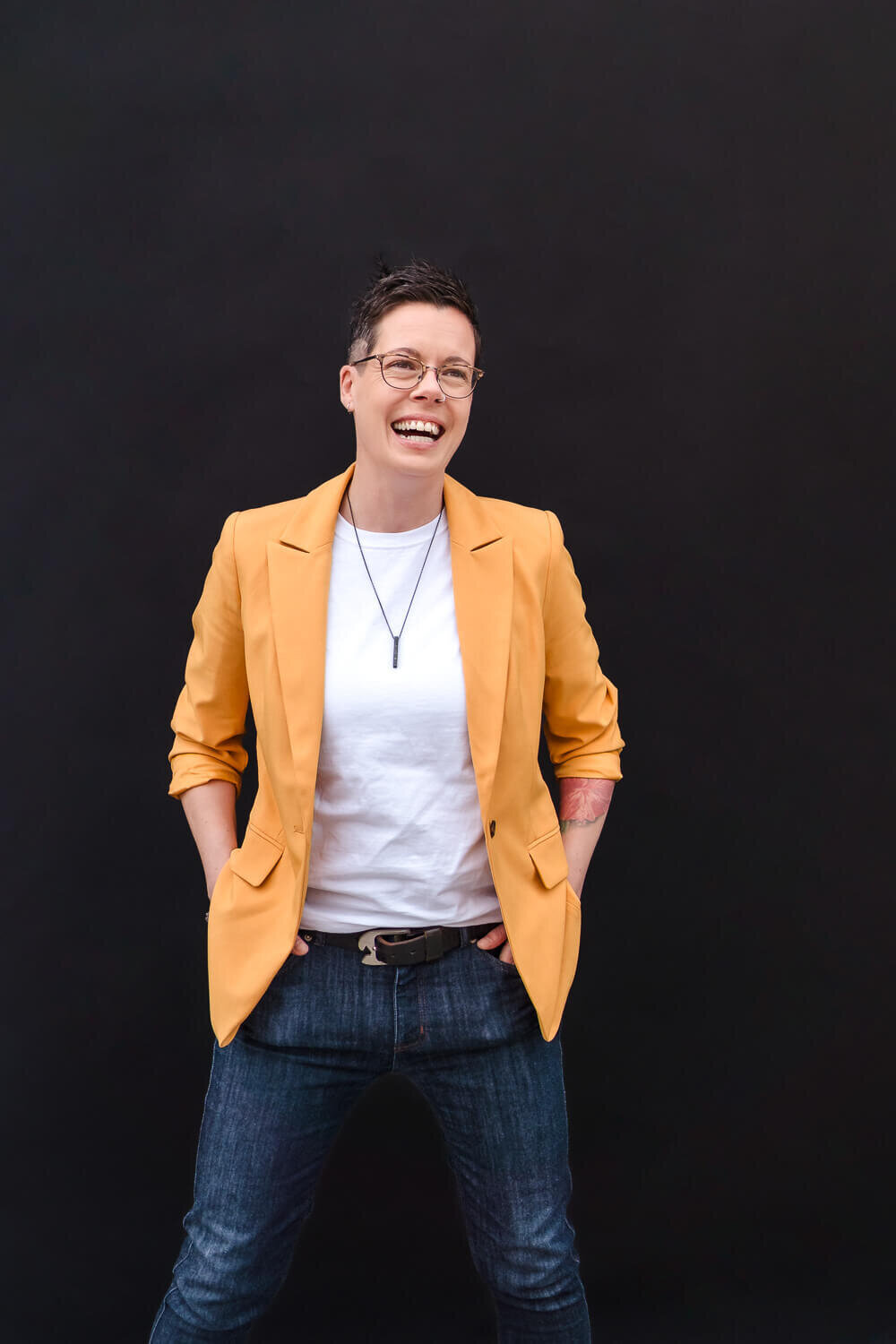 Smiling business woman in yellow suit jacket and jeans against a black backdrop