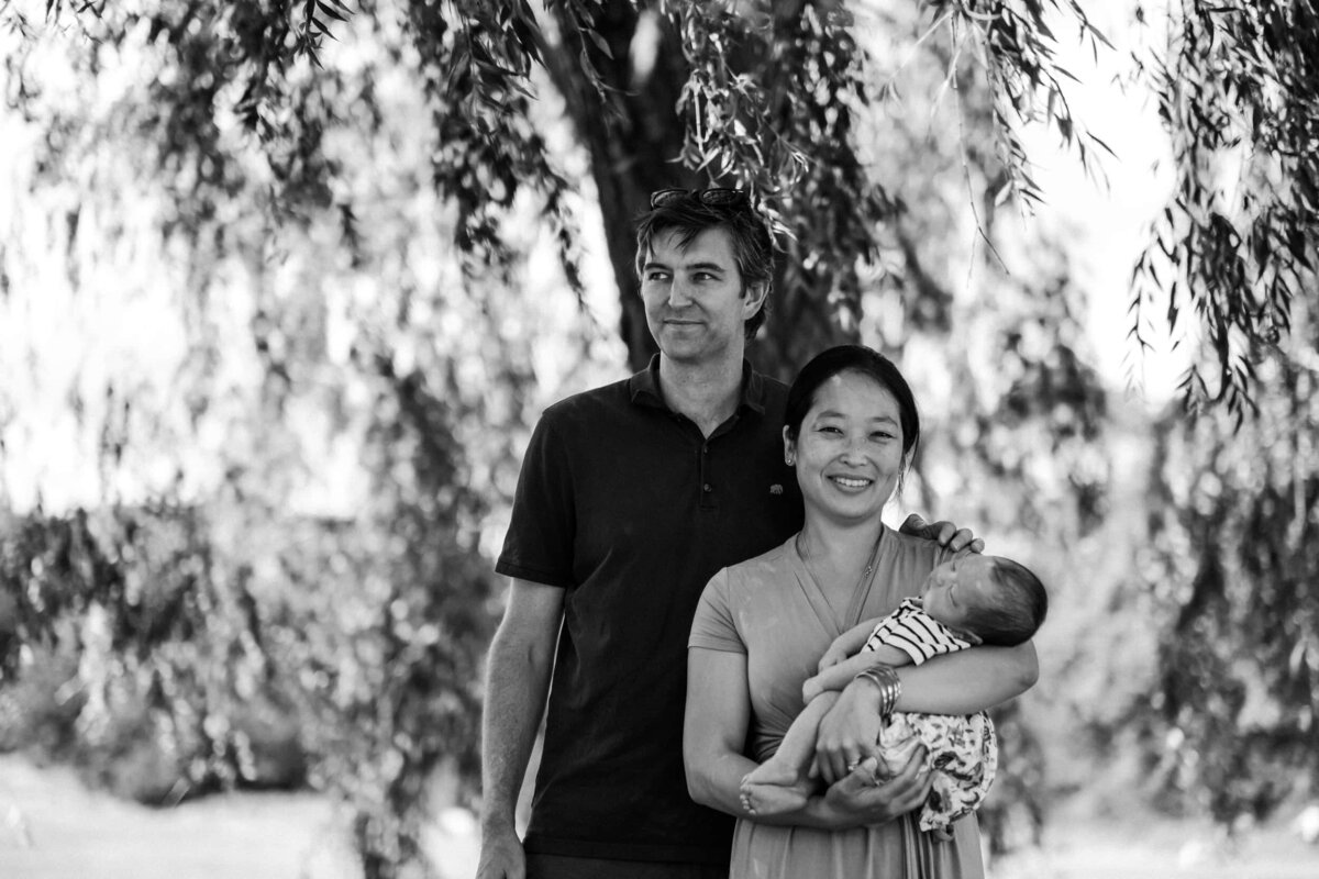 Mother, father and newborn baby stand in front of willow tree at park in London
