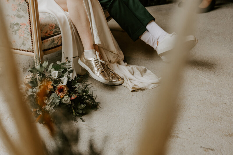 Zoom sur les chaussures des mariés assis dans un canapé ancien et le bouquet de la marié. Photo issus du shooting photo de mariage en Vendée.