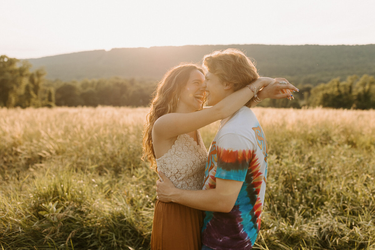 couple with their arms wrapped around each other smiling as the sun sets