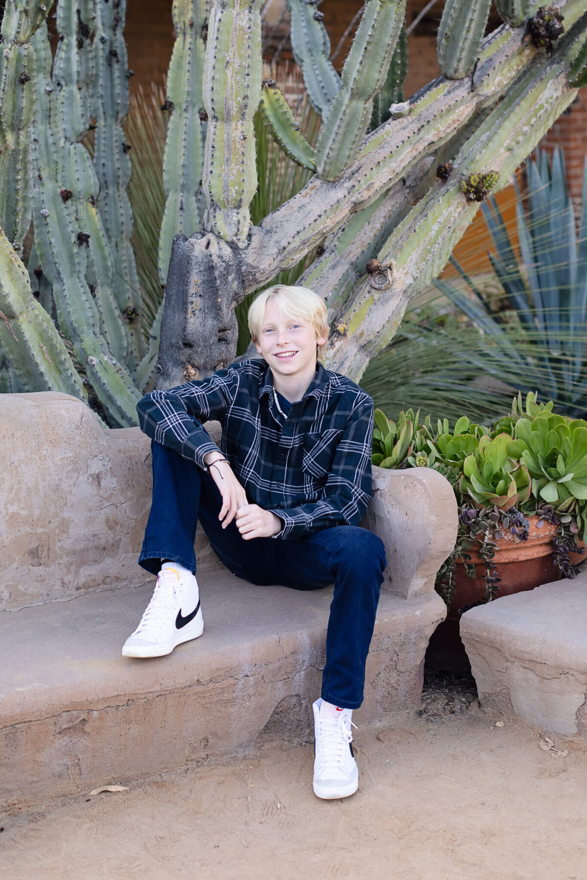 A teen boy with blonde hair sitting on a bench and resting his arm over his knee at San Juan Capistrano.