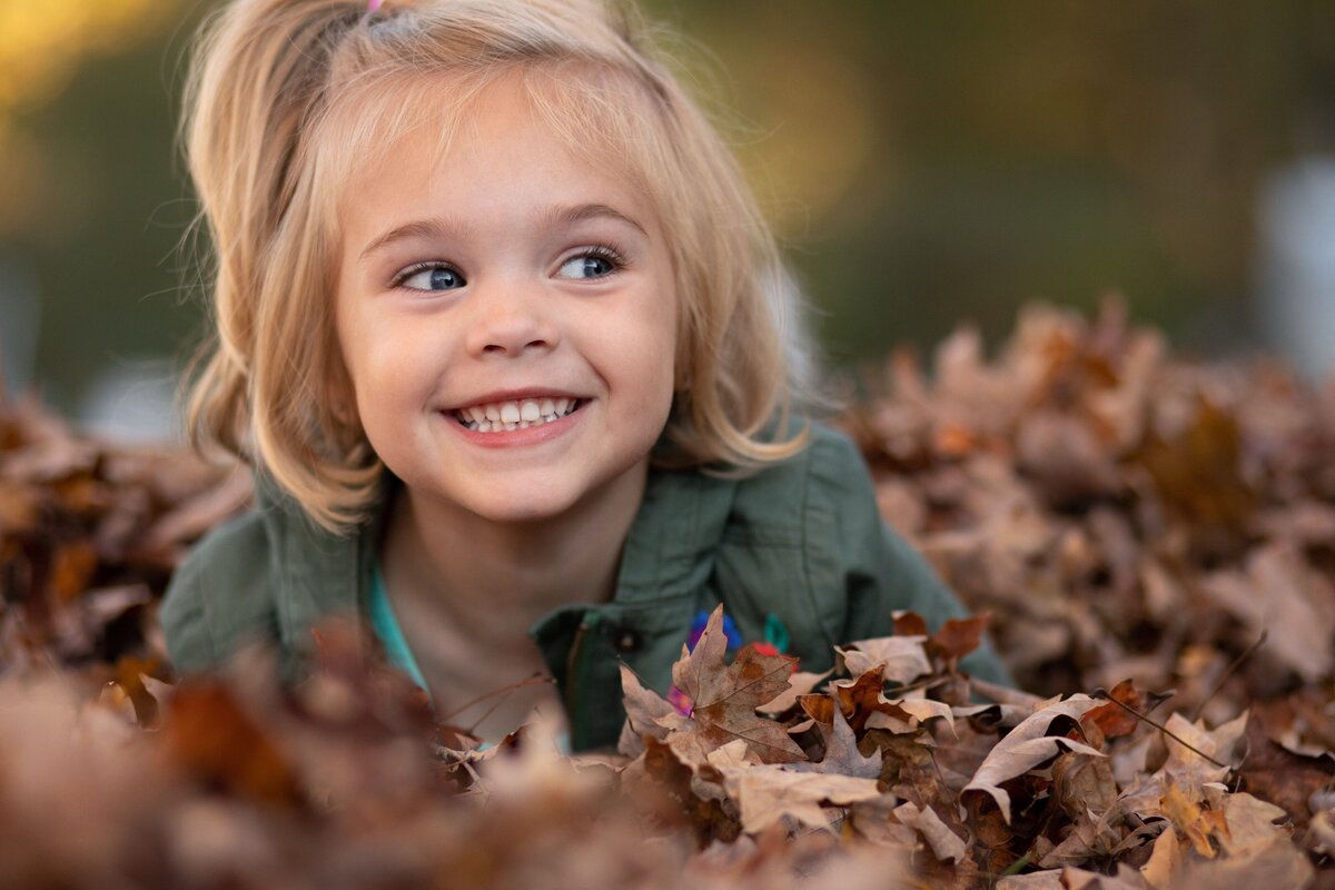 a girl smiling in a pile of leaves
