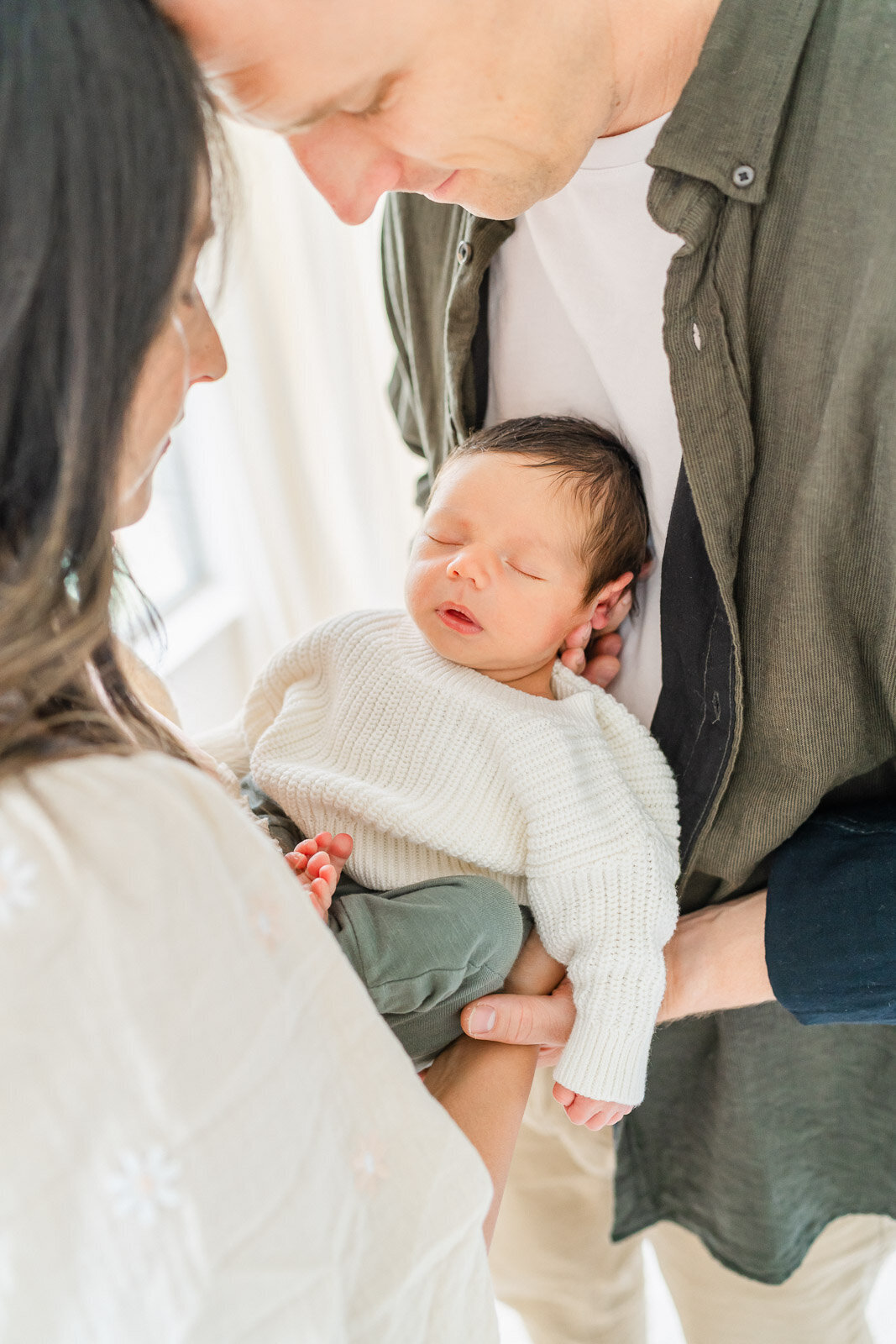 an infant boy rests on the chest of his father while held by his mother.