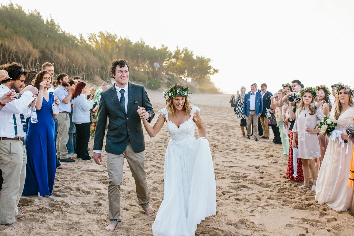 Newlyweds walk down the beach while being cheered on by wedding guests. 