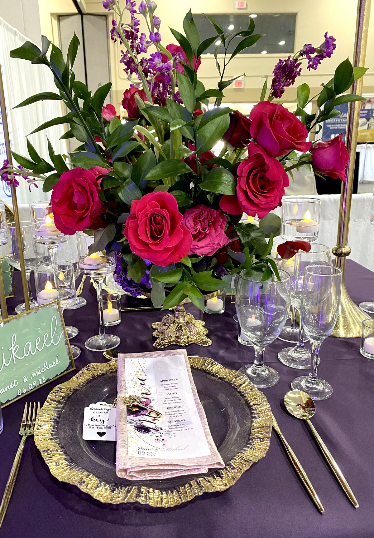 Elegant red floral centerpiece with lush greenery, complemented by glass and gold chargers and a beautifully designed menu card, creating a luxurious tablescape, designed by In Full Bloom Event Planning & Design