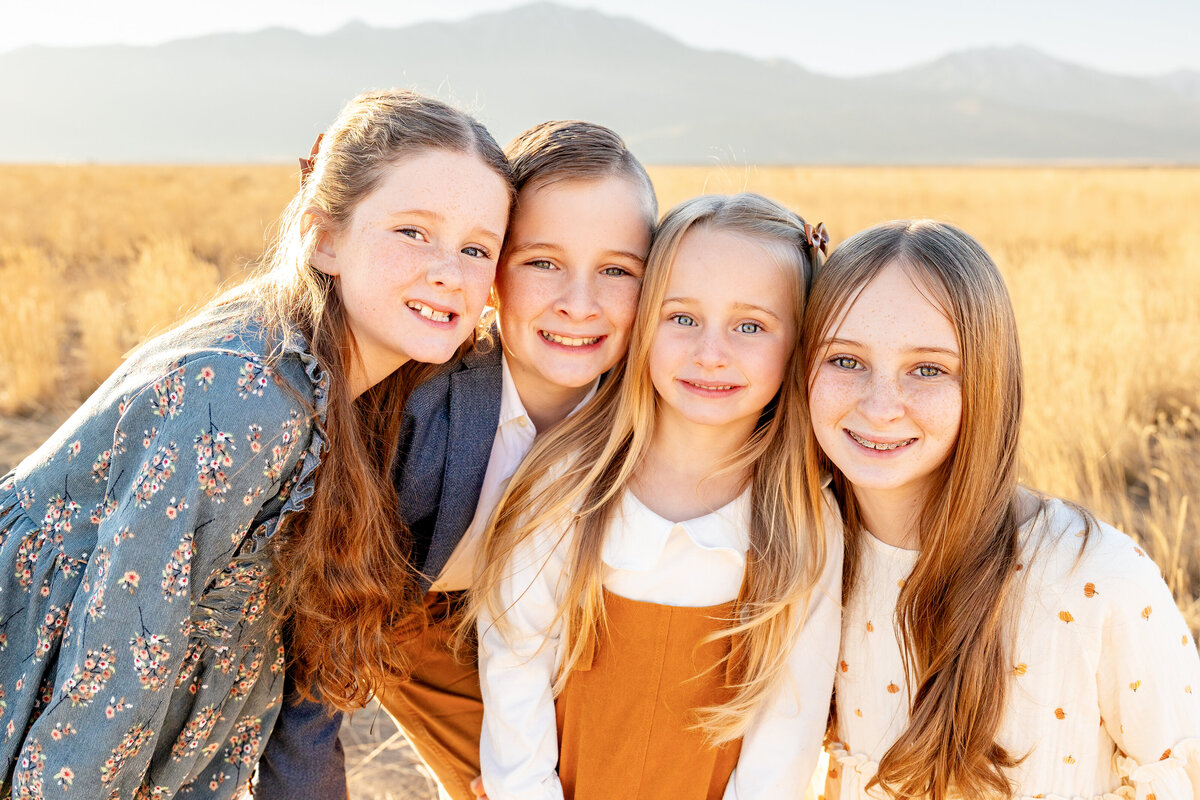 Four siblings pose together in a golden field in Eagle Mountain, Utah, smiling warmly during a sunset family photoshoot by Cassie Lee Photography.