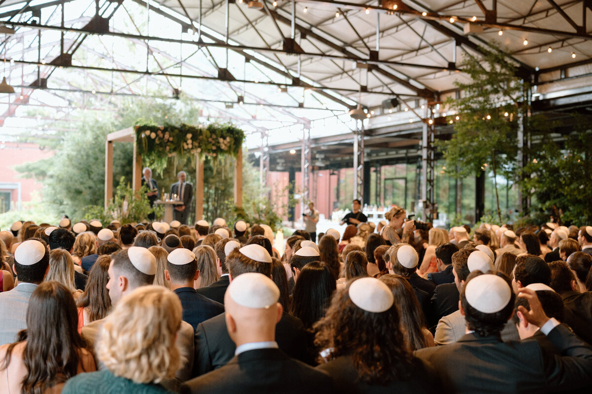 Wide shot of guests wearing kippahs during ceremony under atrium.