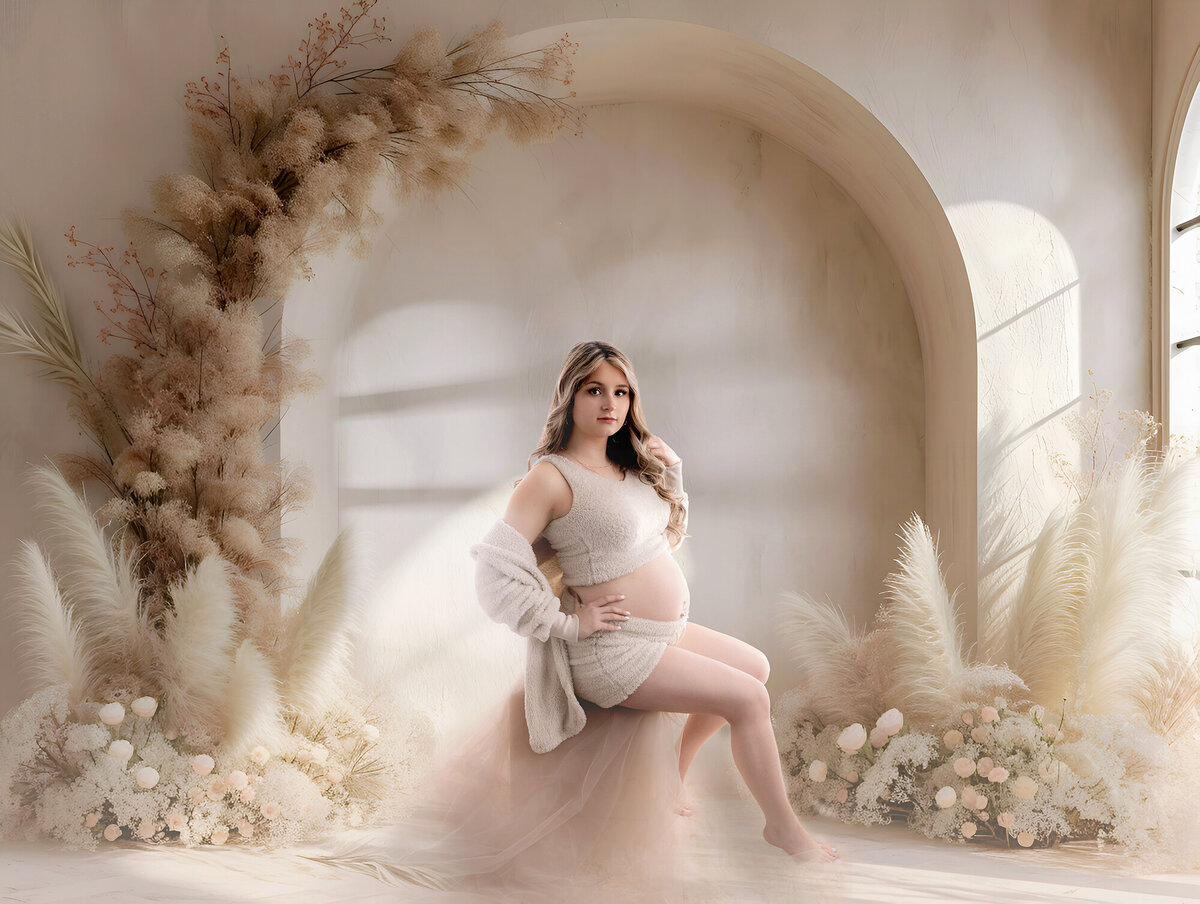 An image from an Iowa maternity photography studio of a mom to be sitting on a block in a boho themed studio