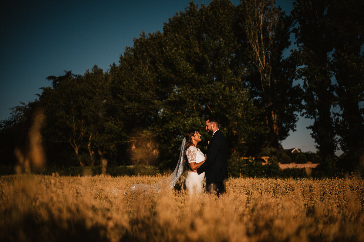 Bride and groom sharing a romantic moment in a sunlit field at Larkspur Lodge wedding venue, surrounded by tall grass and golden light.