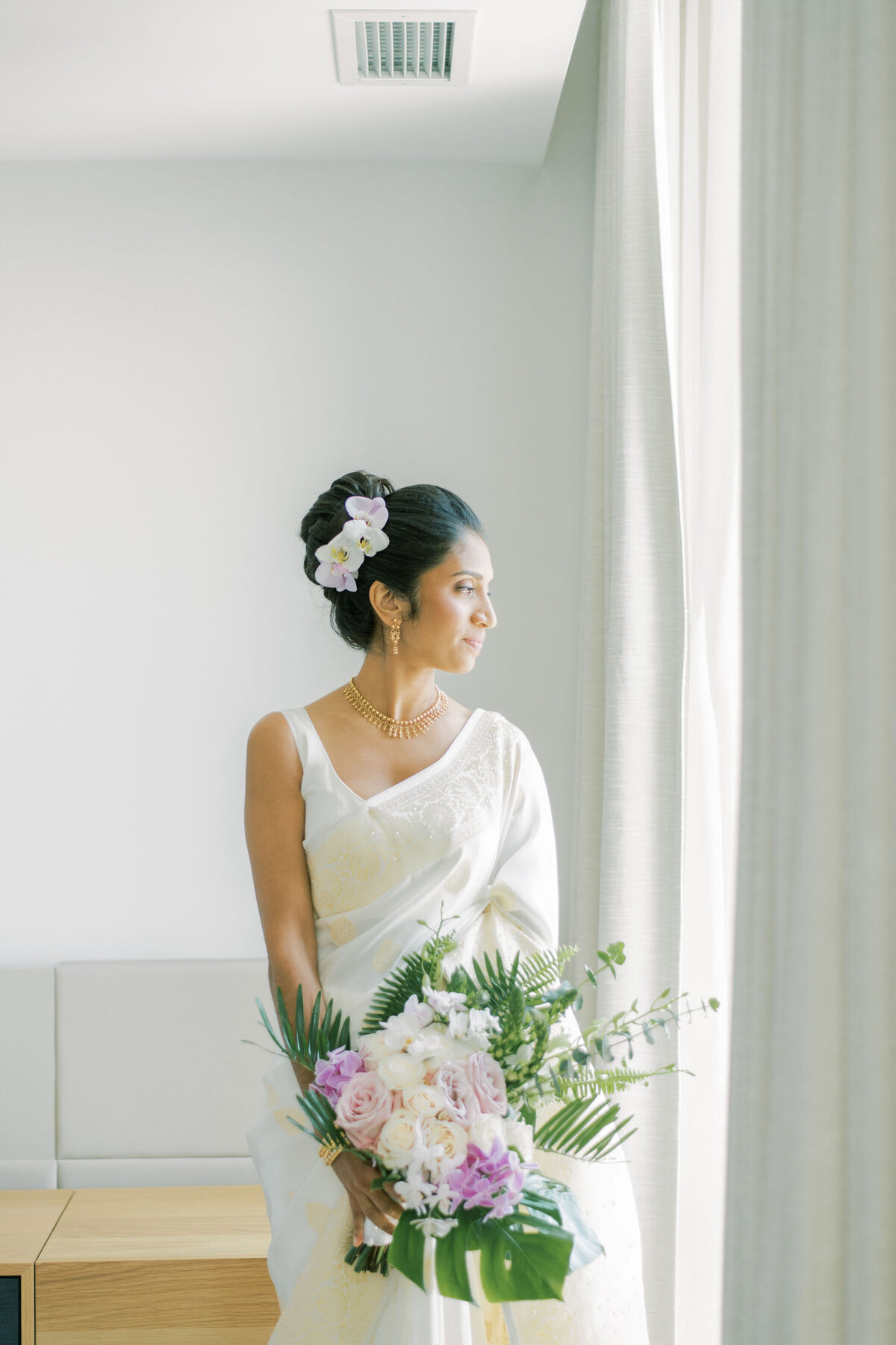 Bride looking out the window  with her flowers in her hand at the pearle hotel