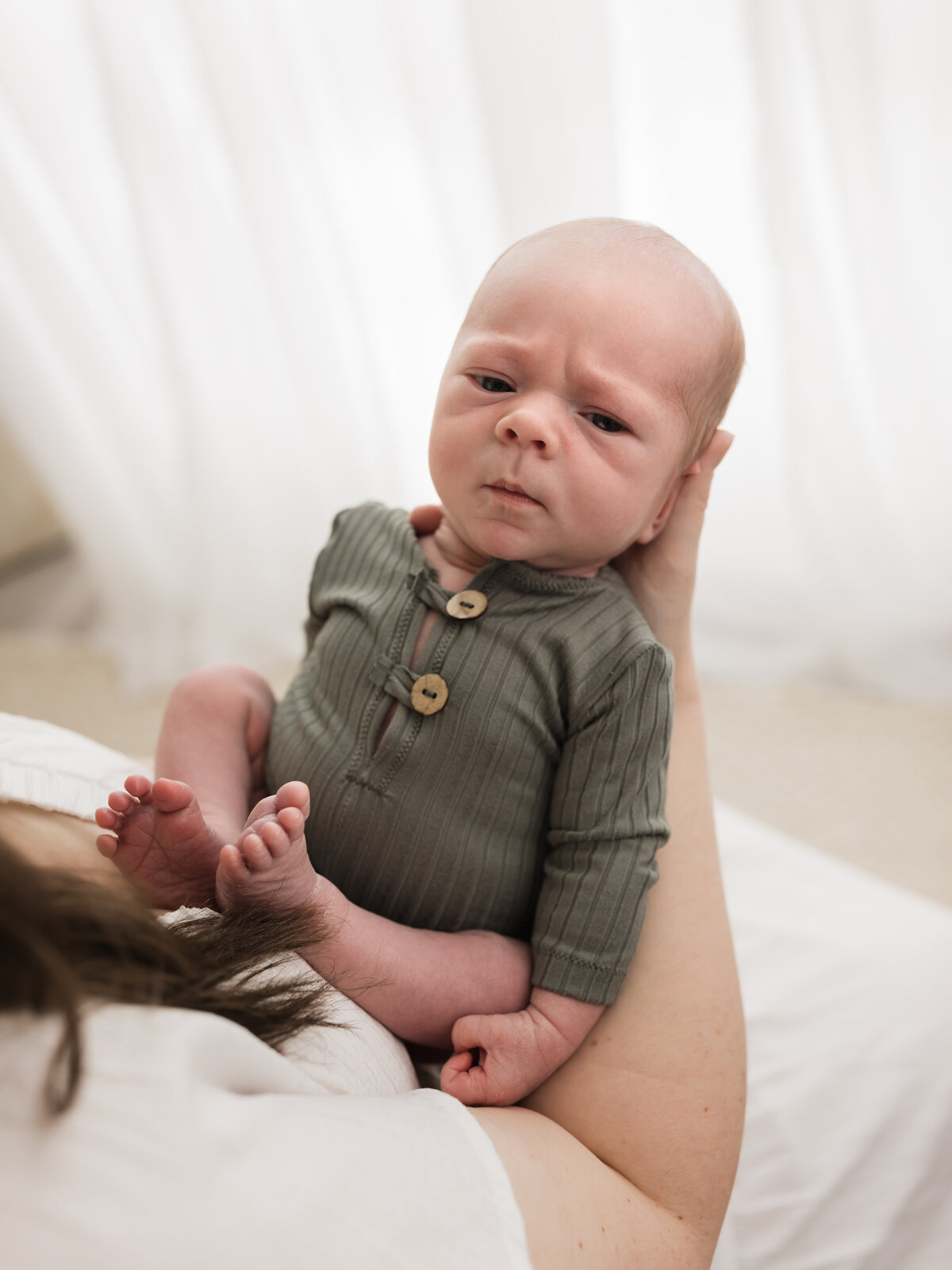 mom holding newborn baby boy in green onesie  for studio portraits in cleveland, ohio