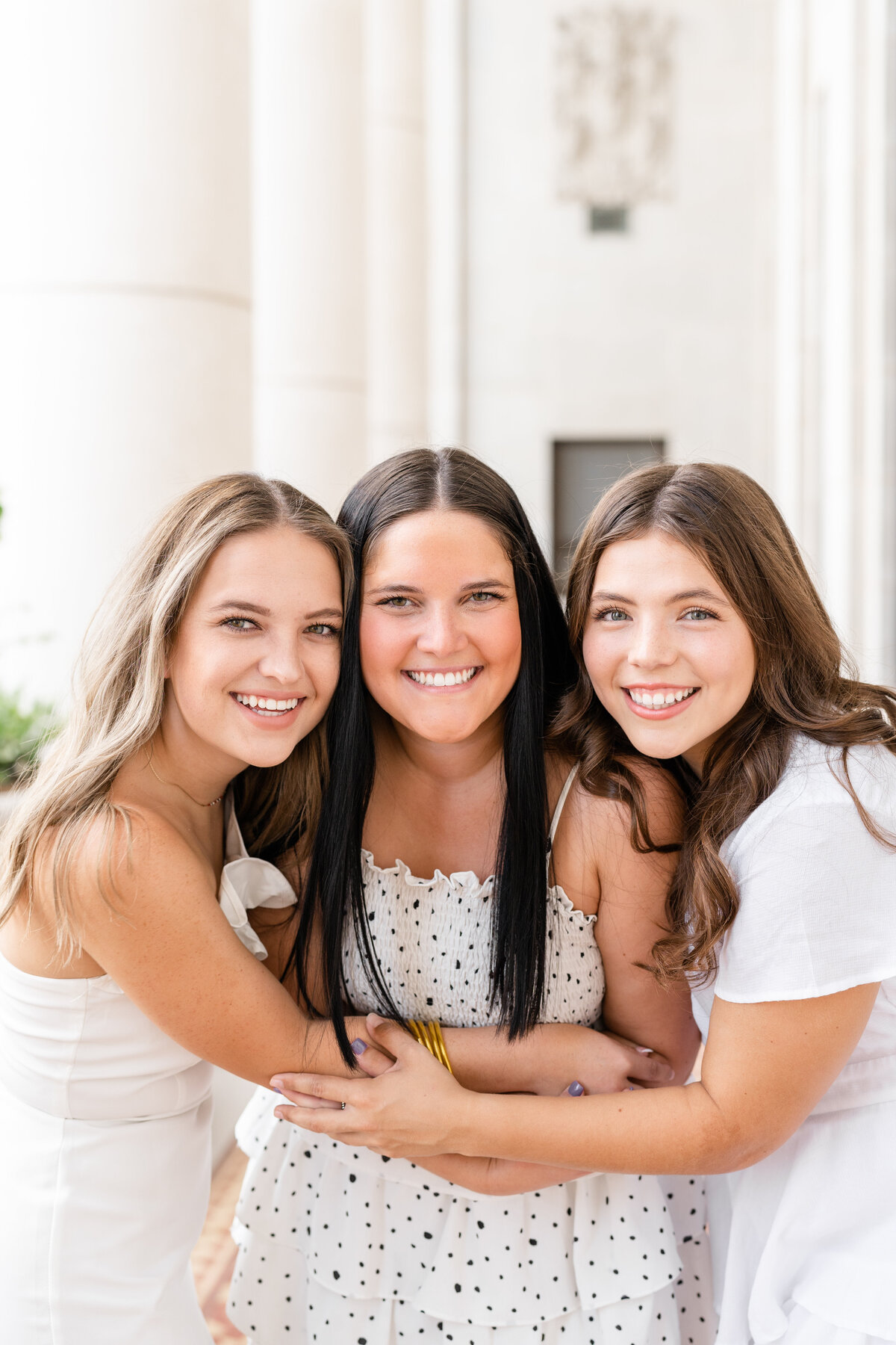 Texas A&M senior girls hugging each other and smiling while wearing white dresses in the columns of the Administration Building
