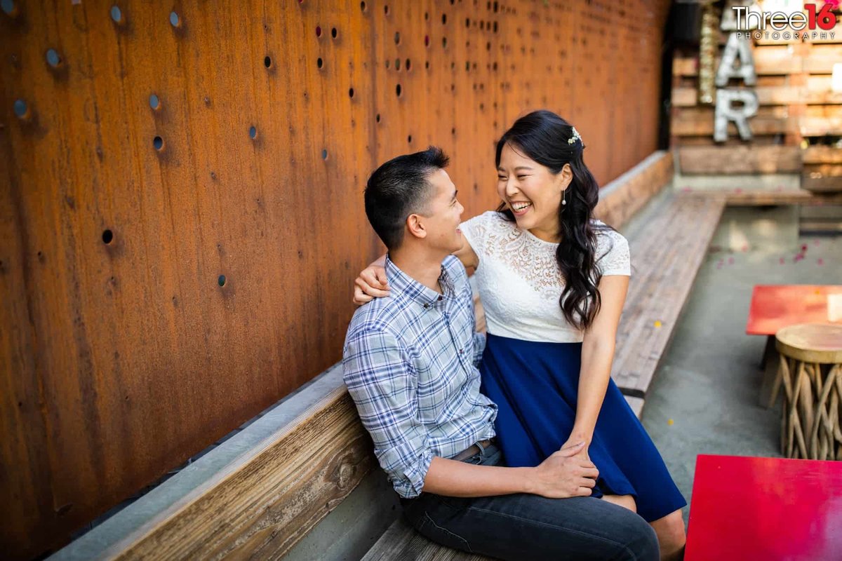 Bride to be sits on her fiance's lap as they gaze into each other's eyes during an Arts District engagement session in Los Angeles